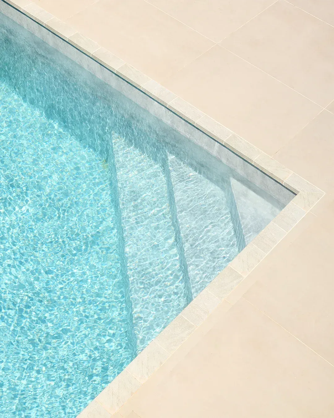 Angle d'une piscine aux eaux turquoise, marches immergées et margelles en pierre claire, photographe immobilier Suisse romande & France