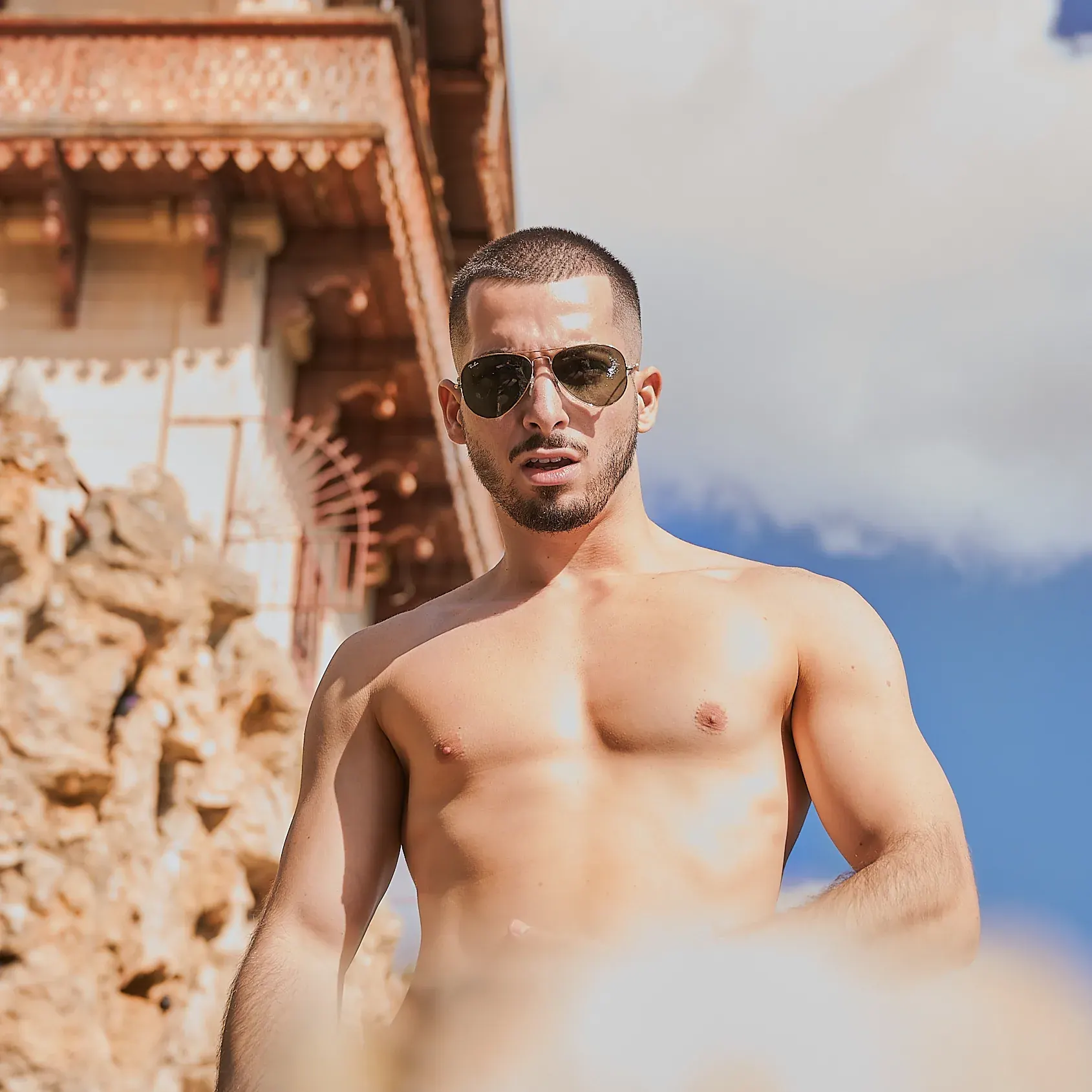Athlète torse nu en lunettes aviateur, pectoraux dessinés en contre-plongée sous ciel bleu, photographe fitness Suisse romande & France