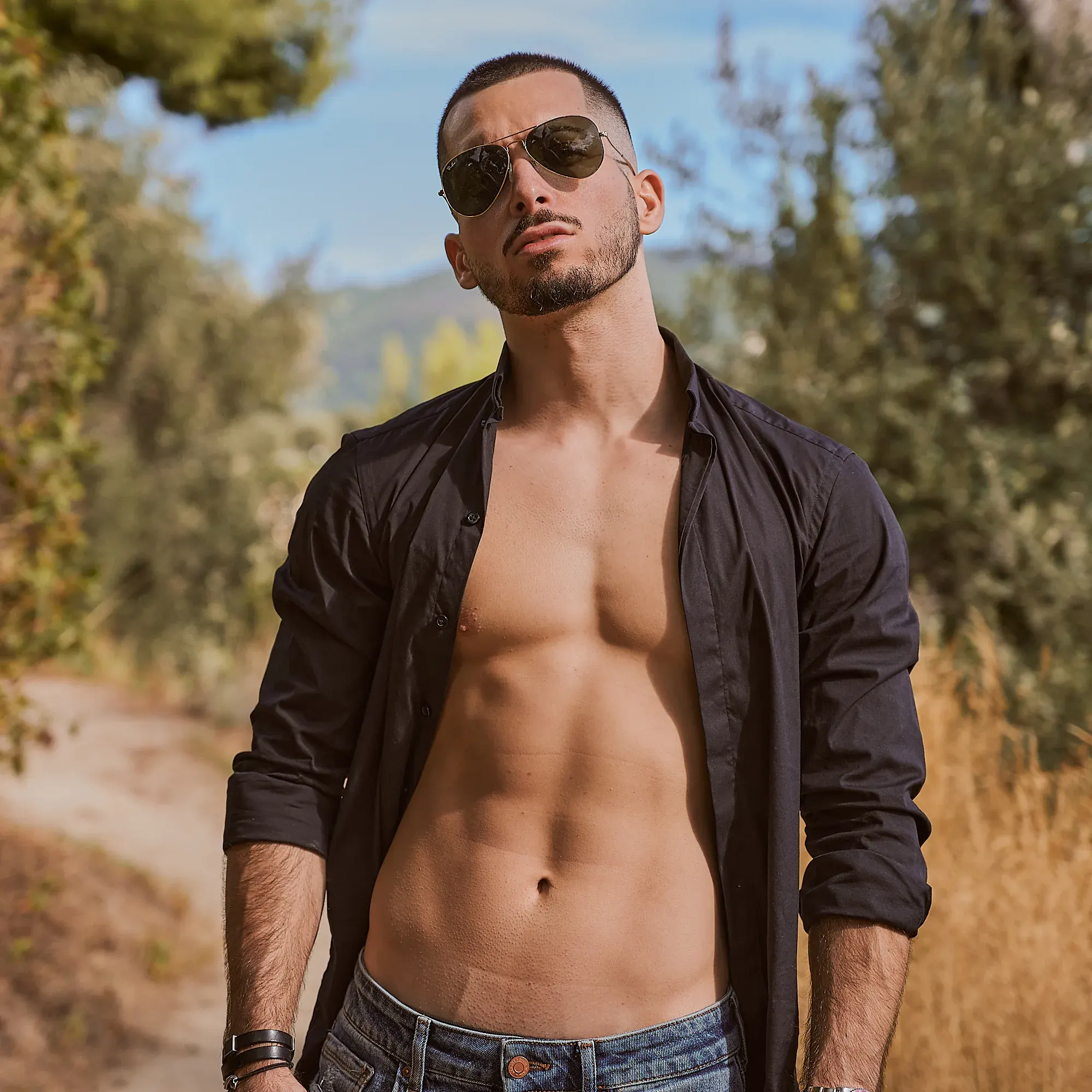Athlète torse nu sous une chemise noire ouverte, abdominaux dessinés, lunettes aviateur, sentier ensoleillé – photographe fitness Suisse romande & France