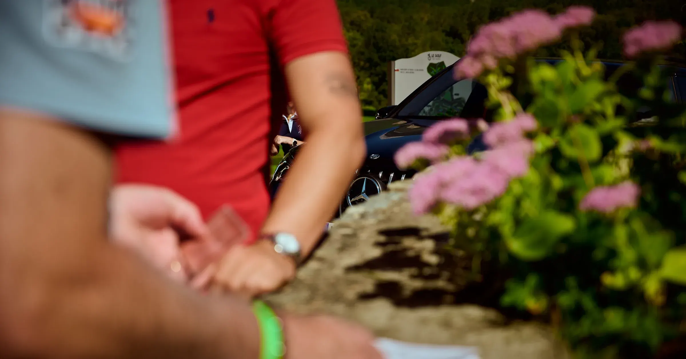 Calandre Mercedes-Benz entre deux golfeurs et des fleurs roses au Golf des Alpes à Giez, photographie automobile