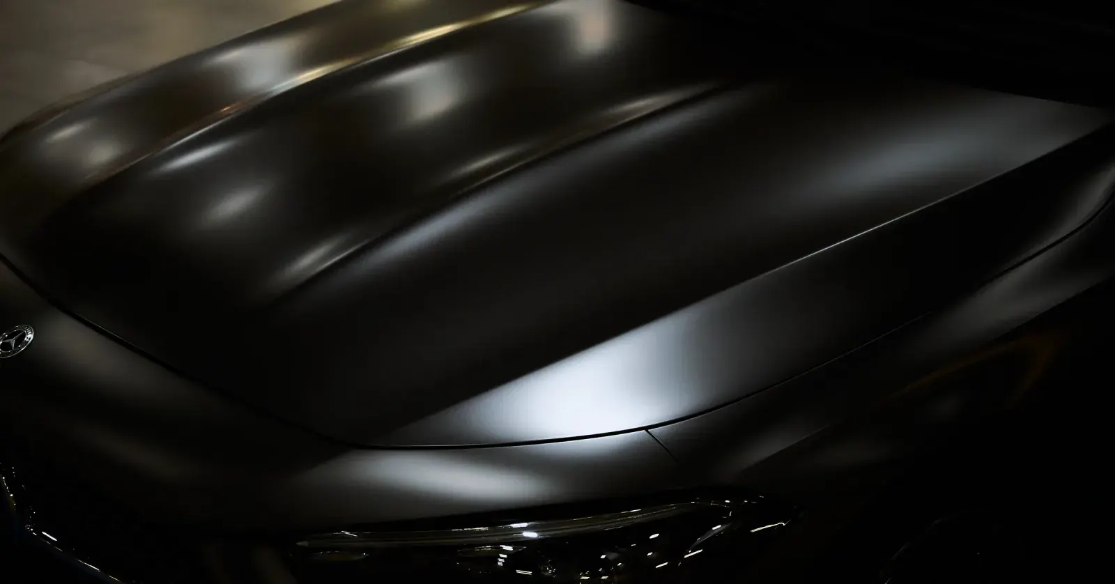 Capot nervuré d’une Mercedes-AMG noire en clair-obscur, le reflet sculptant la
ligne plutôt que la
hacher