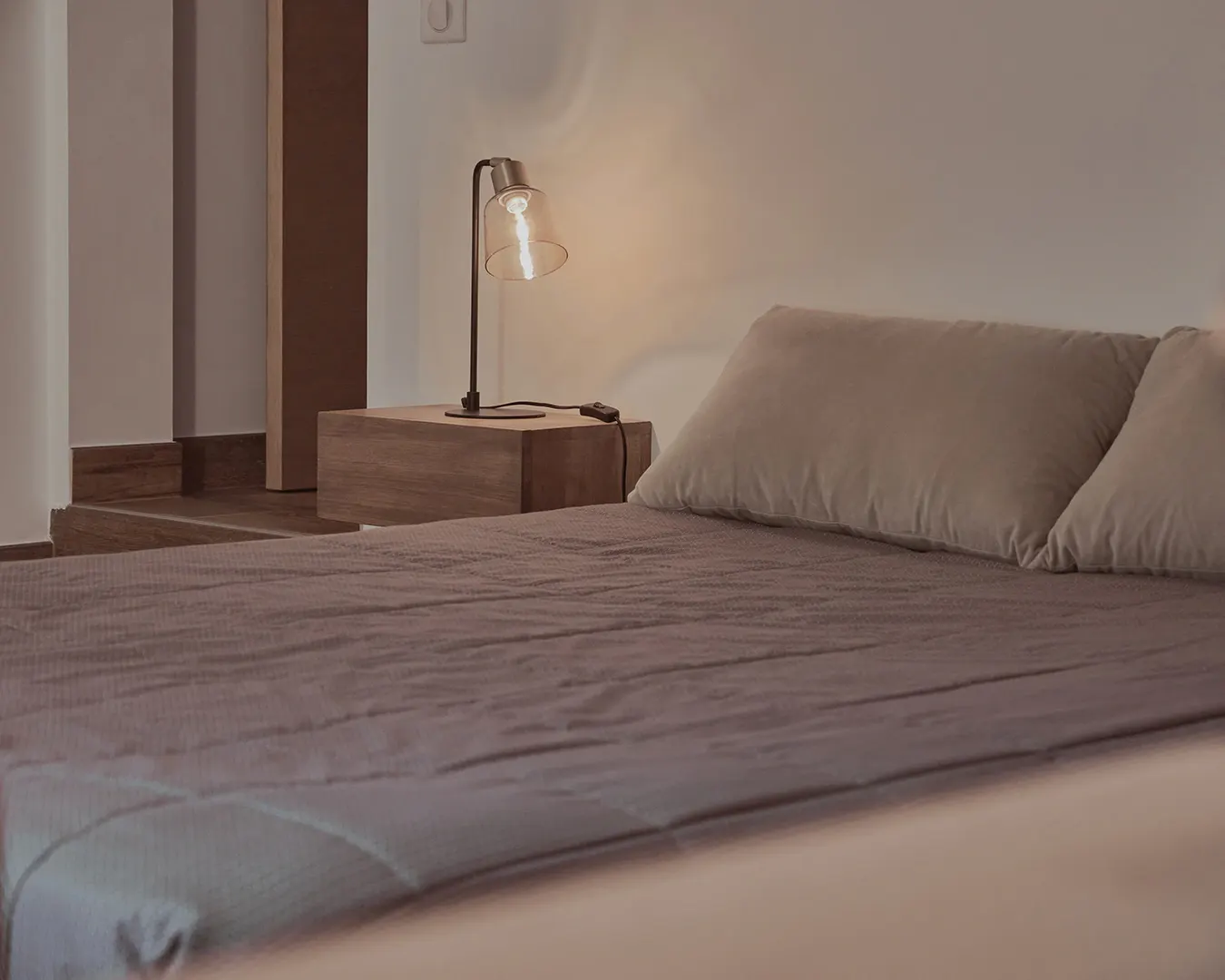 Chambre épurée aux tons beige, lit double et lampe de chevet allumée, photographie immobilière d’intérieur