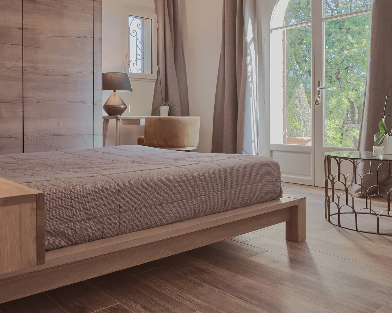 Chambre principale aux tons bois et lin, baie vitrée ouverte sur jardin, photographie immobilière en Suisse romande
