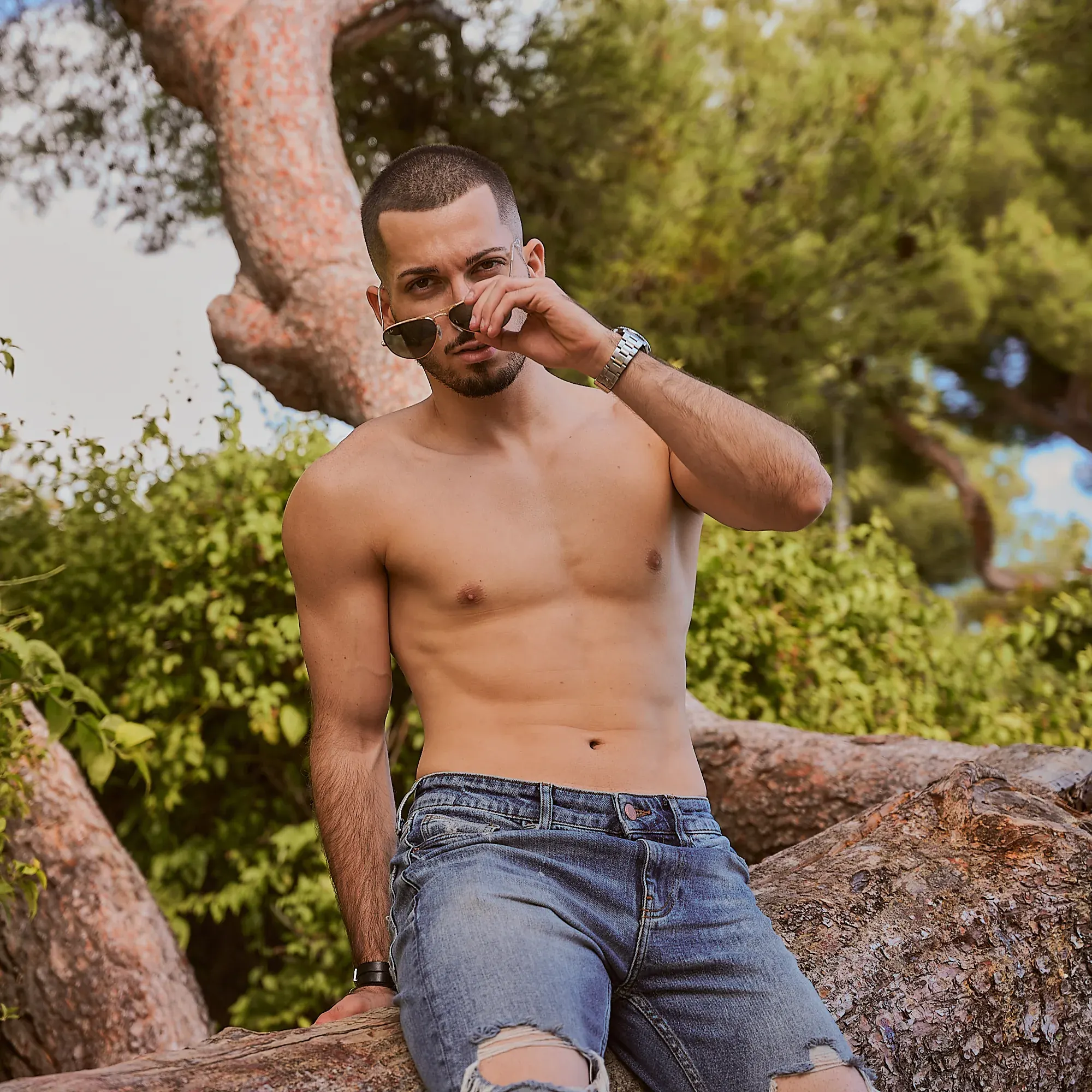 Coach fitness torse nu en jean, lunettes aviateur baissées, assis sur un tronc de pin, photographe fitness Suisse romande & France