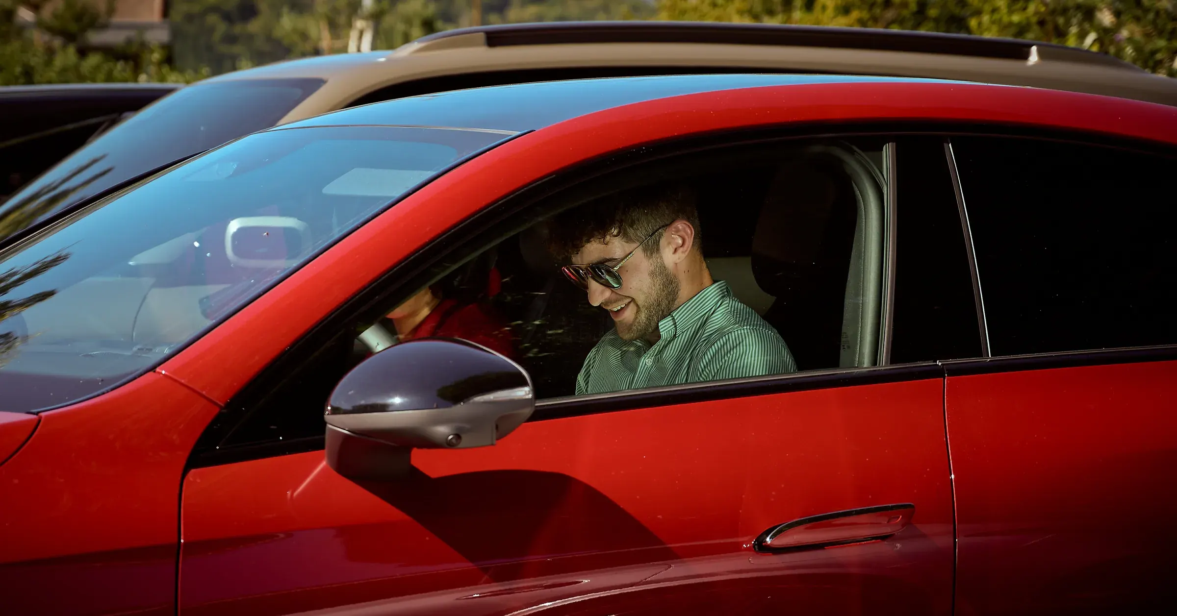 Conducteur souriant en chemise rayée au volant d'un SUV rouge, reportage automobile au Golf des Alpes à Giez