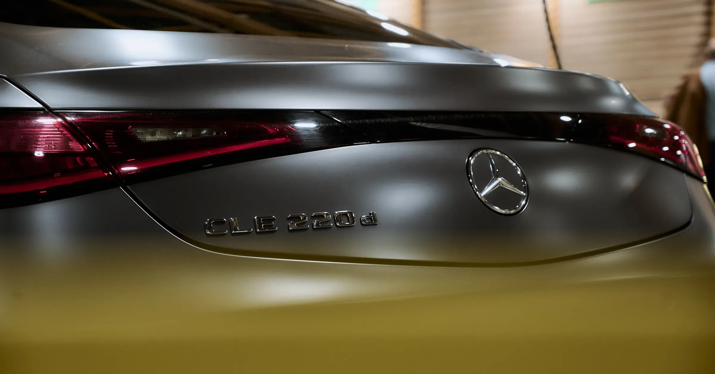 Coffre gris mat d’une Mercedes-Benz CLE 220d, étoile chromée, monogramme et feux LED rouges : photographe automobile à La Roche-sur-Foron