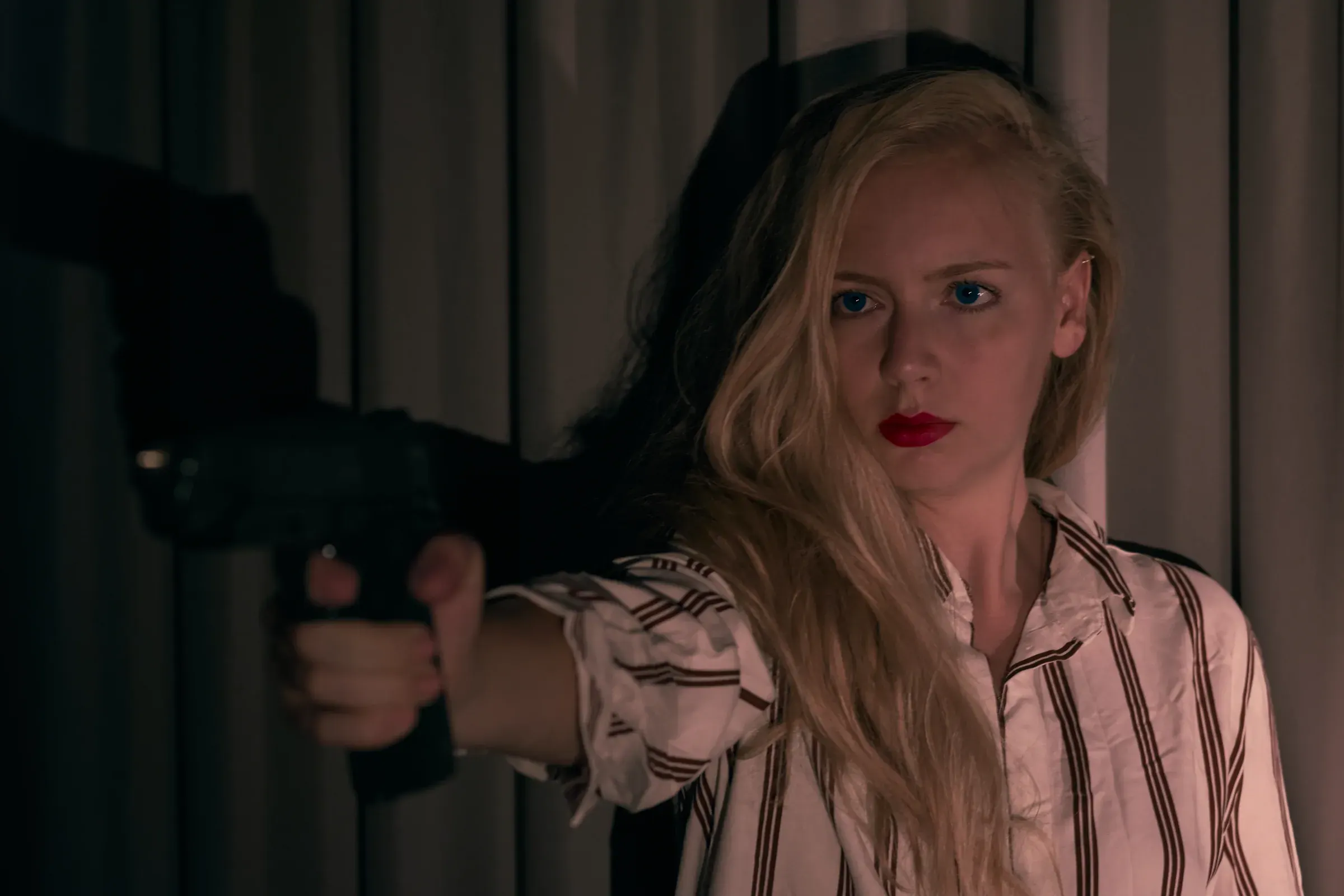 Femme blonde aux lèvres rouges en chemise rayée qui pointe un pistolet vers l'objectif, portrait mis en scène à Annecy