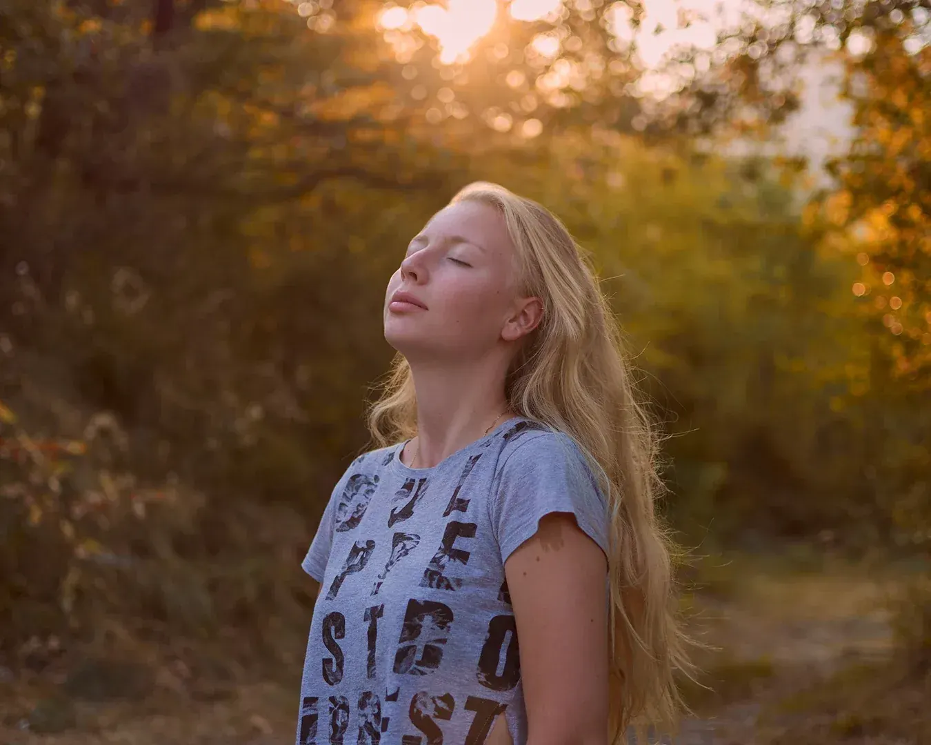 Jeune femme blonde aux yeux clos, visage tourné vers le soleil couchant, portrait en lumière naturelle par photographe à Nice