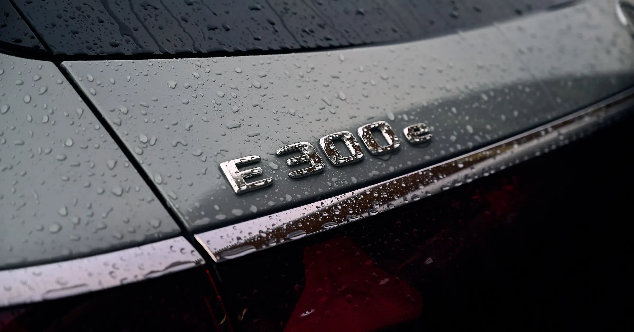 Monogramme chromé E 300 e sur le coffre gris perlé de pluie d'une Mercedes-Benz, photographe automobile à La Roche-sur-Foron