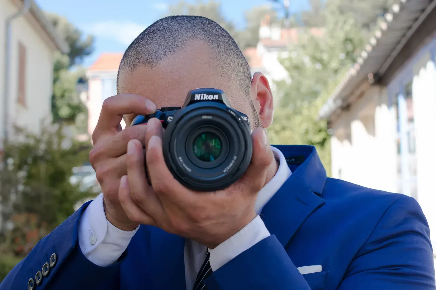 Pierre Vie en costume bleu, l'œil dans le viseur d'un Nikon D3500, photographe professionnel sur la Côte d'Azur