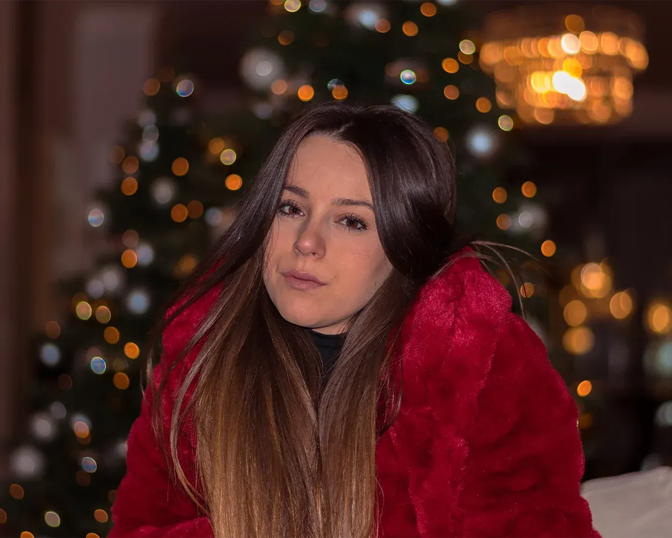 Portrait d'une jeune femme brune en manteau rouge, regard direct devant un sapin illuminé, photographe portrait à Nice