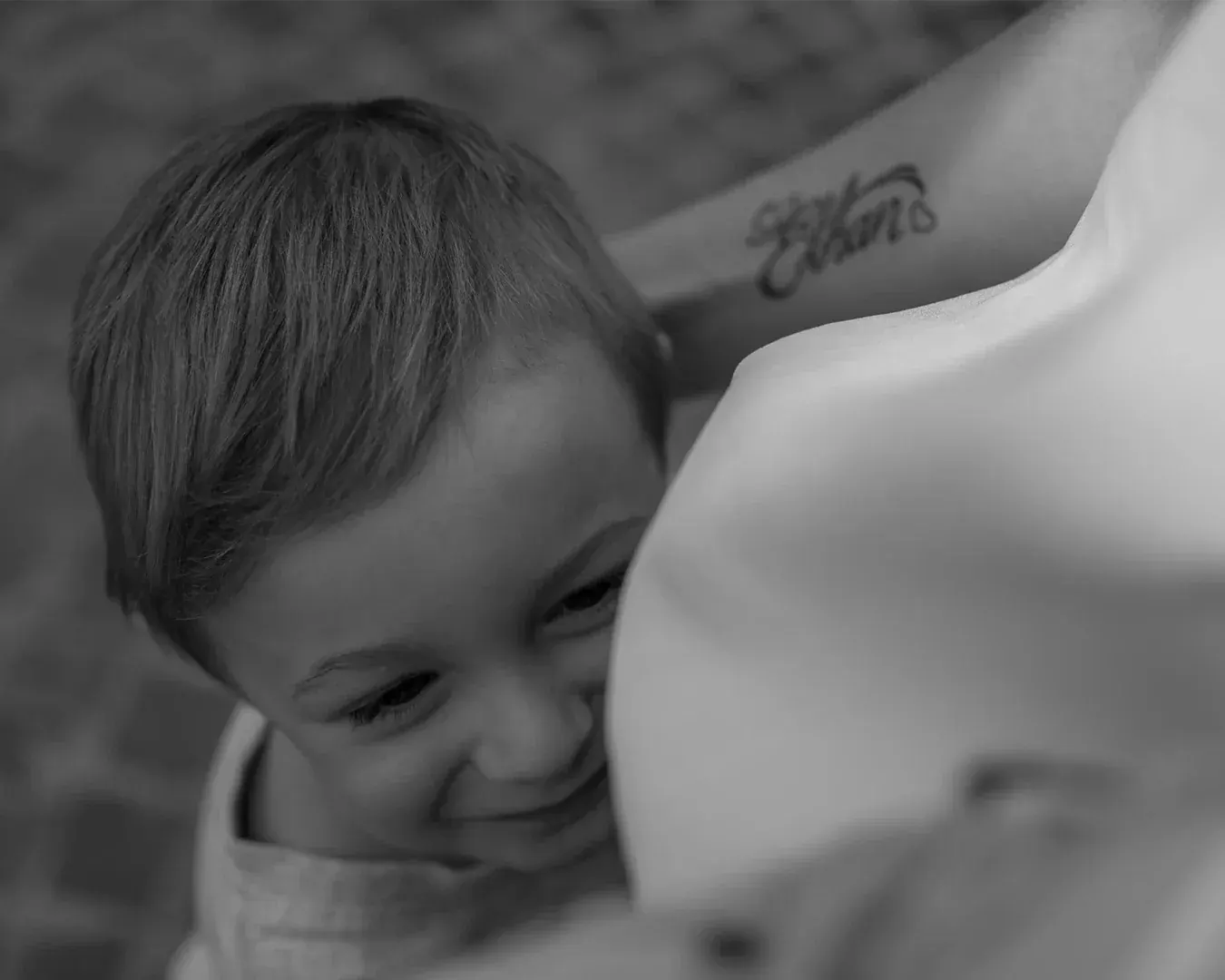 Portrait de famille noir et blanc, jeune enfant rieur blotti contre l'épaule d'un parent, photographe portrait à Nice