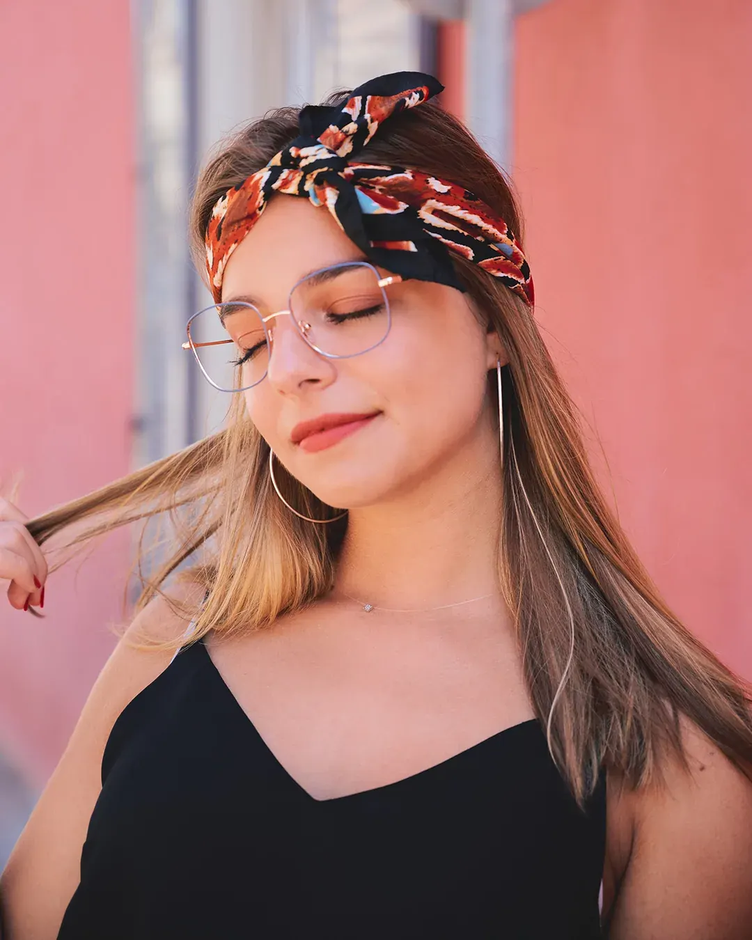 Portrait féminin en extérieur, foulard imprimé et lunettes fines devant un mur rose, lumière naturelle de la Côte d’Azur