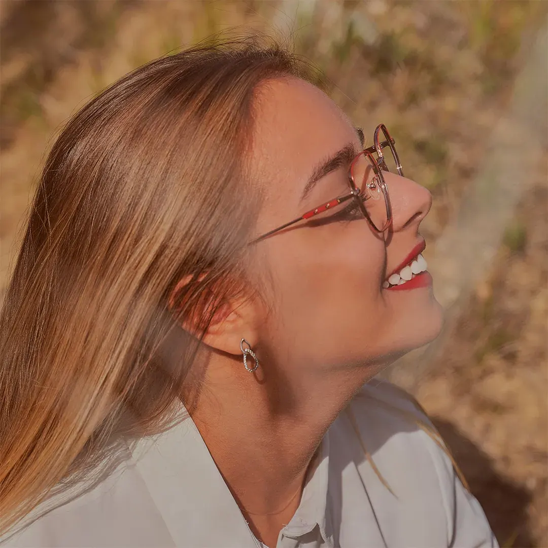 Portrait féminin de profil, sourire et lunettes fines, lumière dorée de fin de journée en extérieur, par un photographe portraitiste
