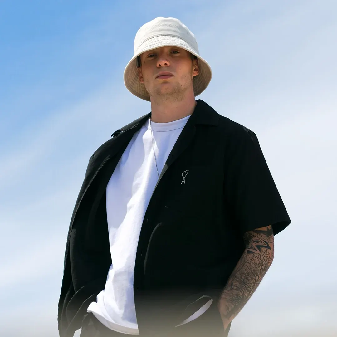 Portrait mode d’un homme au bob blanc et chemise noire ouverte, contre-plongée sur ciel bleu, Côte d’Azur