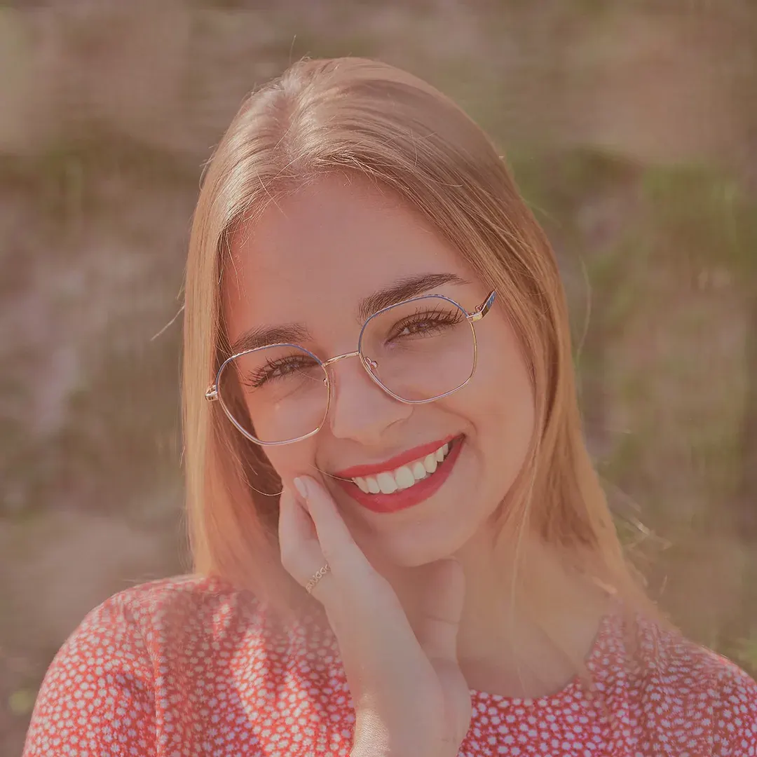 Portrait souriant d’une jeune femme blonde à lunettes en robe fleurie rouge, lumière dorée en extérieur
