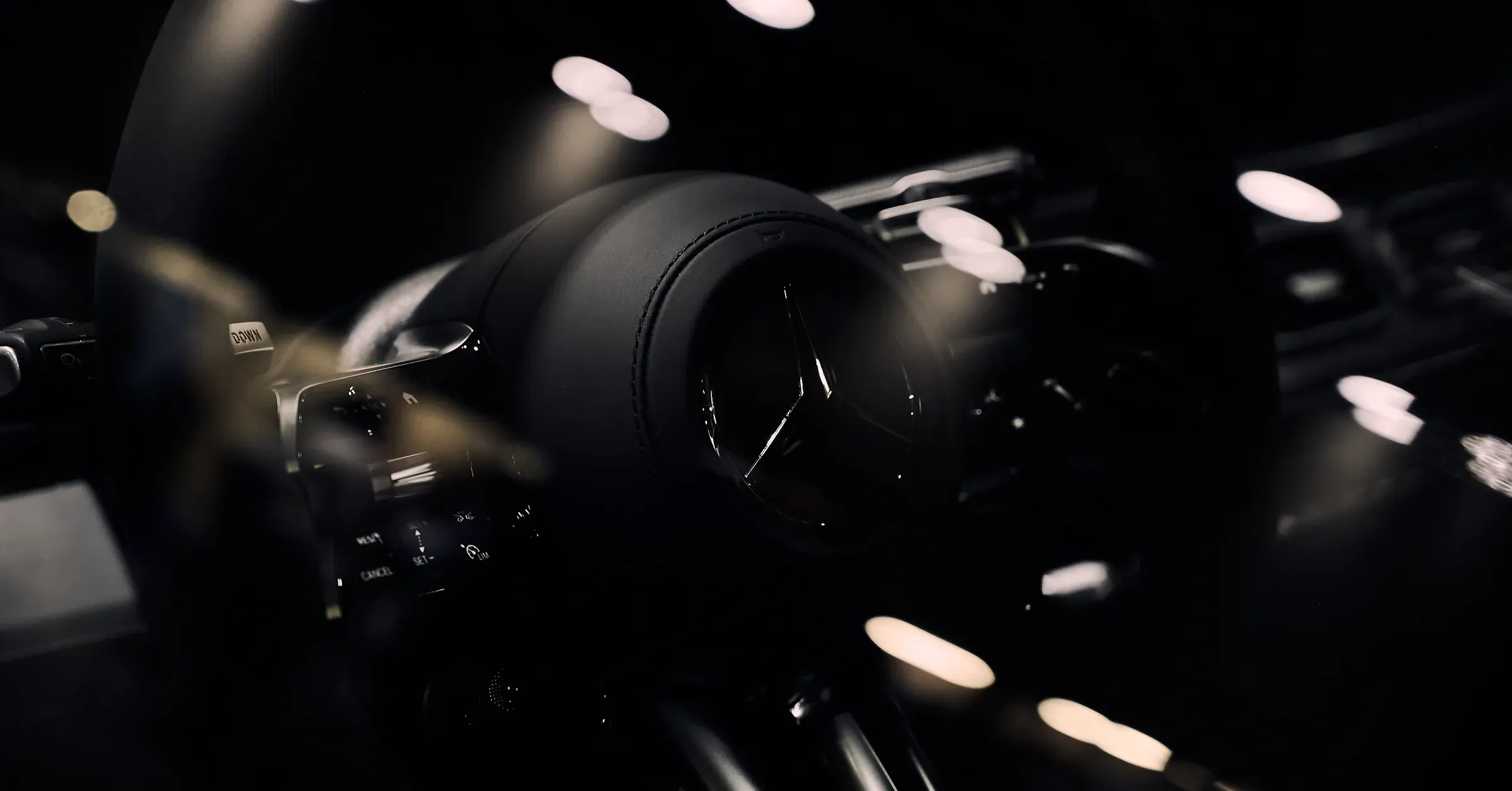 Volant en cuir noir surpiqué d'une Mercedes-Benz, étoile et palette DOWN en clair-obscur, bokeh doré – photographe automobile